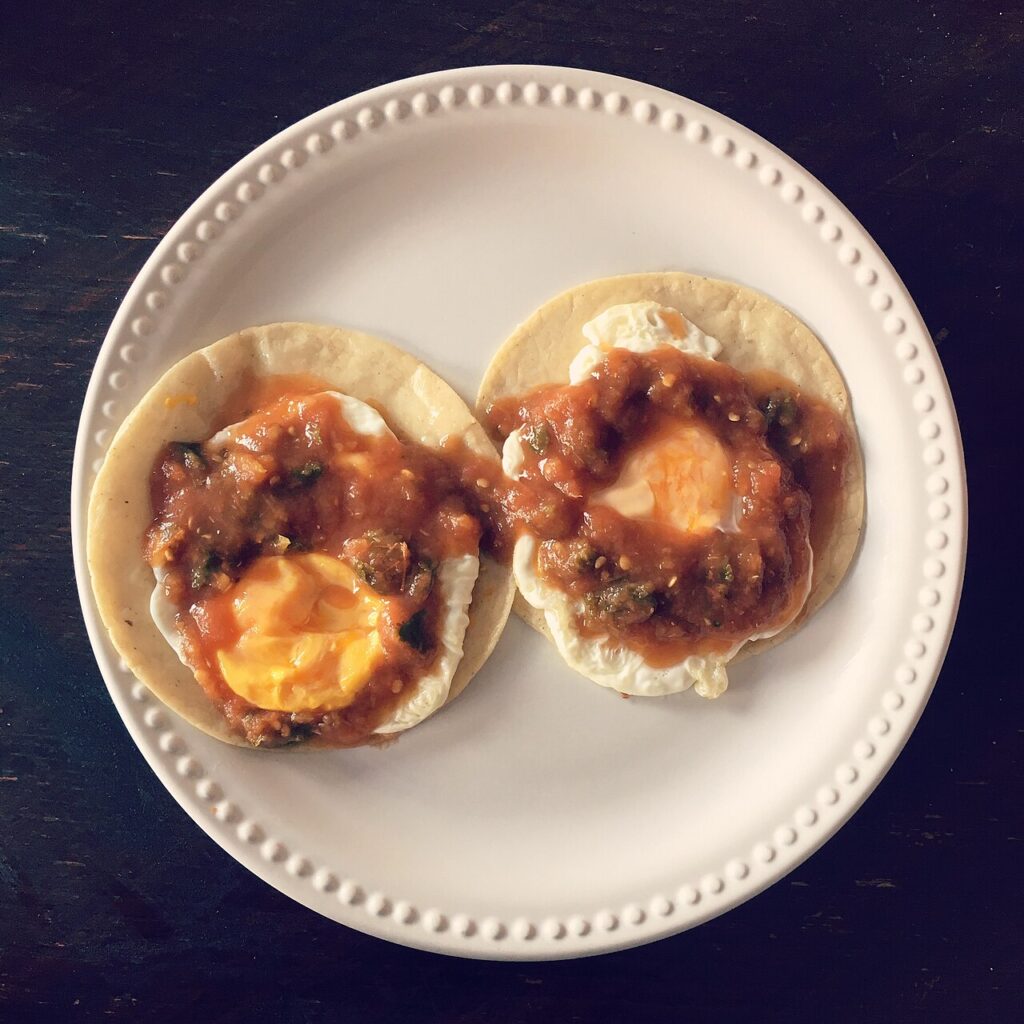 Huevos rancheros sobre tortilla frita bañados en salsa roja