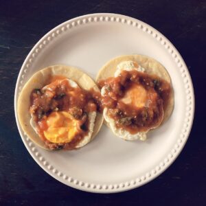 Huevos rancheros sobre tortilla frita bañados en salsa roja