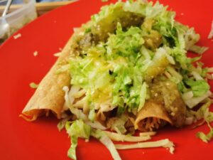 Tacos dorados de pollo con lechuga, crema y queso